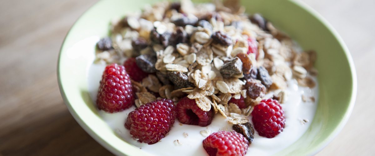 A bowl of yogurt topped with raspberries and dried fruit