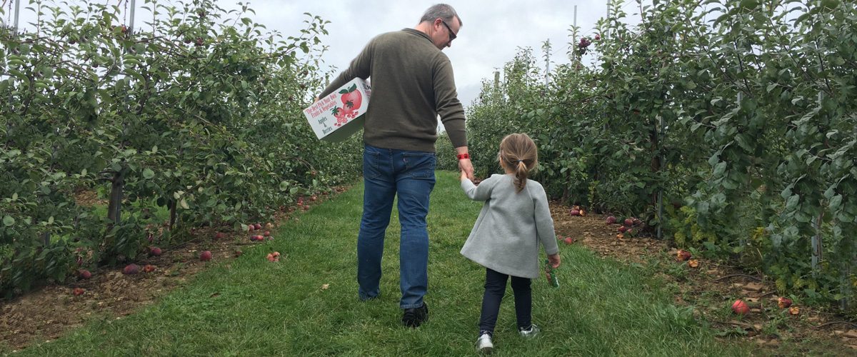 A photo of Peter McKay and his daughter walking through an apple grove