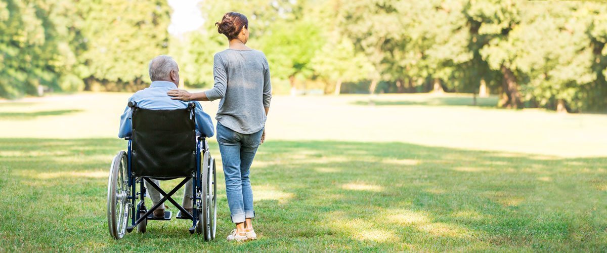 An elderly man in a wheelchair and a young woman standing next to him