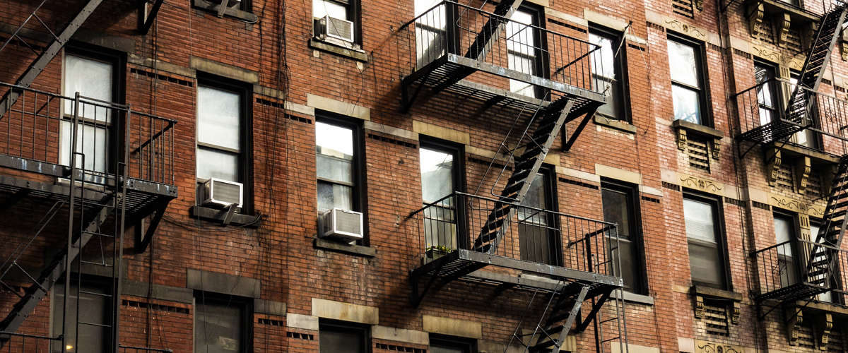 Exterior of apartment building with lots of windows and fire escapes.