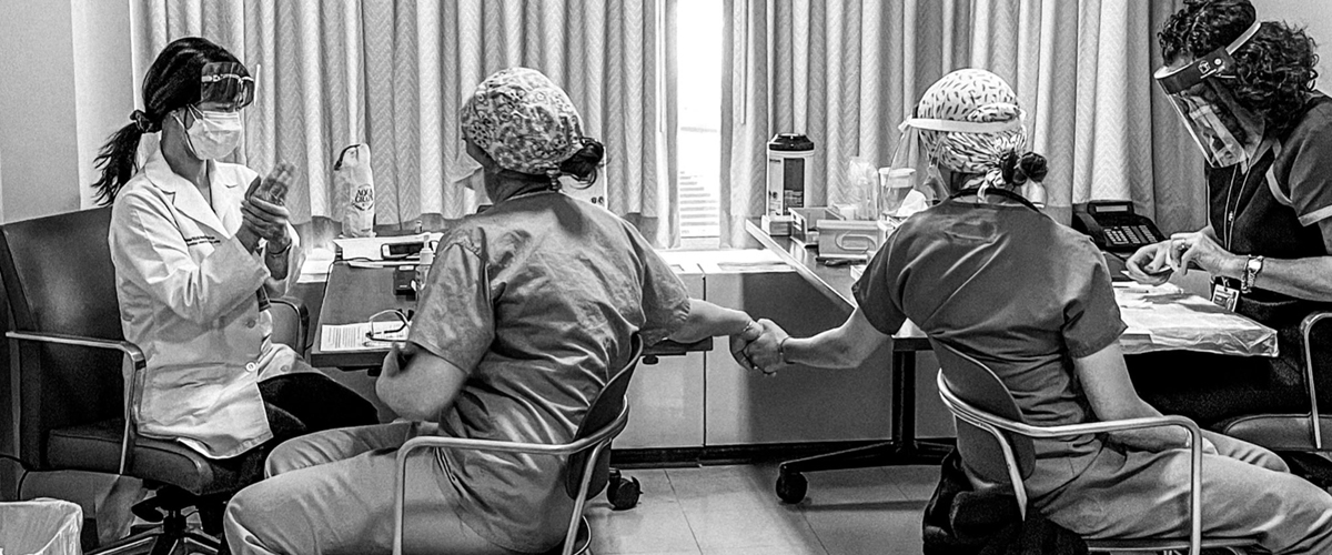 Two healthcare workers holding hands while receiving the COVID-19 vaccine